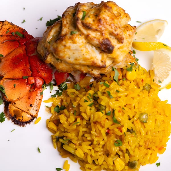 The Manor's New American dish featuring a lobster tail, stuffed chicken, yellow rice, and lemon wedges.