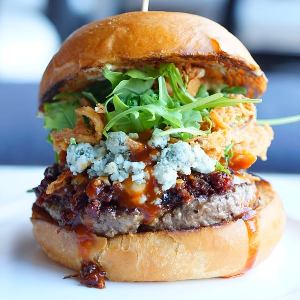Gourmet burger with blue cheese, crispy onions, arugula, and a rich sauce on a brioche bun.