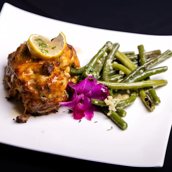 New-American chicken dish with green beans, lemon, and a purple orchid on a white plate.